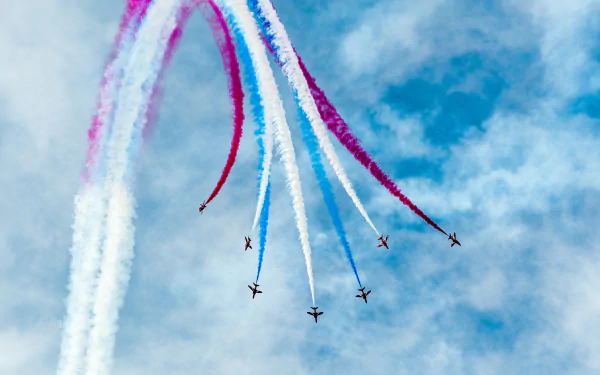 Six military airplanes perform a colorful air show, trailing red, white, and blue smoke against a clear blue sky in this 4K Ultra HD desktop wallpaper.