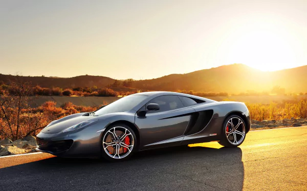 Silver McLaren MP4-12C supercar parked on a road at sunset, with a desert landscape in the background, captured in HD for a desktop wallpaper.