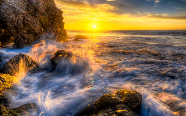 4K Ultra HD wallpaper capturing Malibu’s rocky sea cave at sunset, with golden sunlight reflecting on the waves and rugged cliffs along the shore.