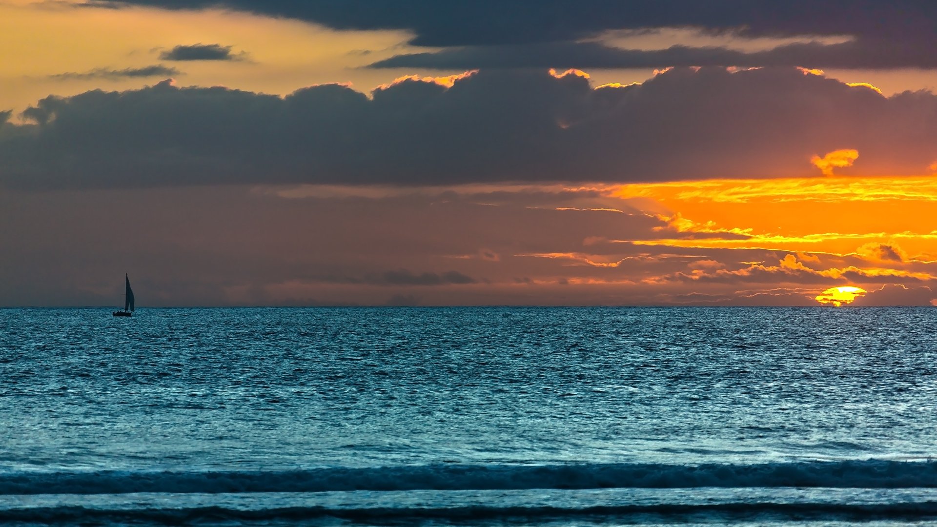 HD PC desktop wallpaper showing a serene ocean under a vibrant sunset sky with a single sailboat on the horizon, capturing the beauty of nature.