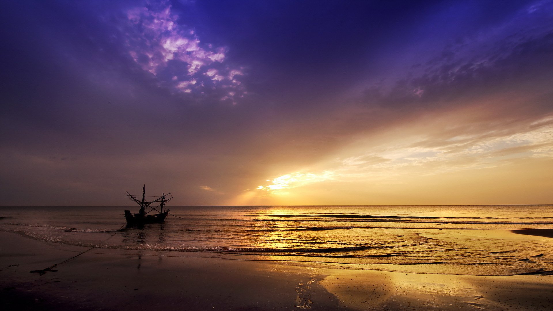 A serene beach at sunset with a small boat silhouetted against a vibrant purple and golden sky, captured in HD for a nature-themed PC desktop wallpaper.