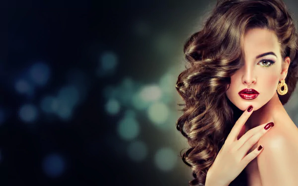 A glamorous woman with elegant curls and bold red lipstick poses gracefully, showcasing statement earrings against a softly blurred, colorful background. This HD image adds sophistication to any desktop.
