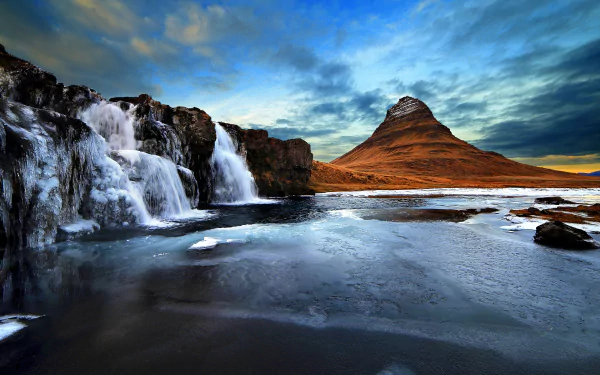 Kirkjufoss waterfall with icy water and Kirkjufell mountain in the background under a dramatic sky in Iceland’s natural landscape, captured in 4K Ultra HD.
