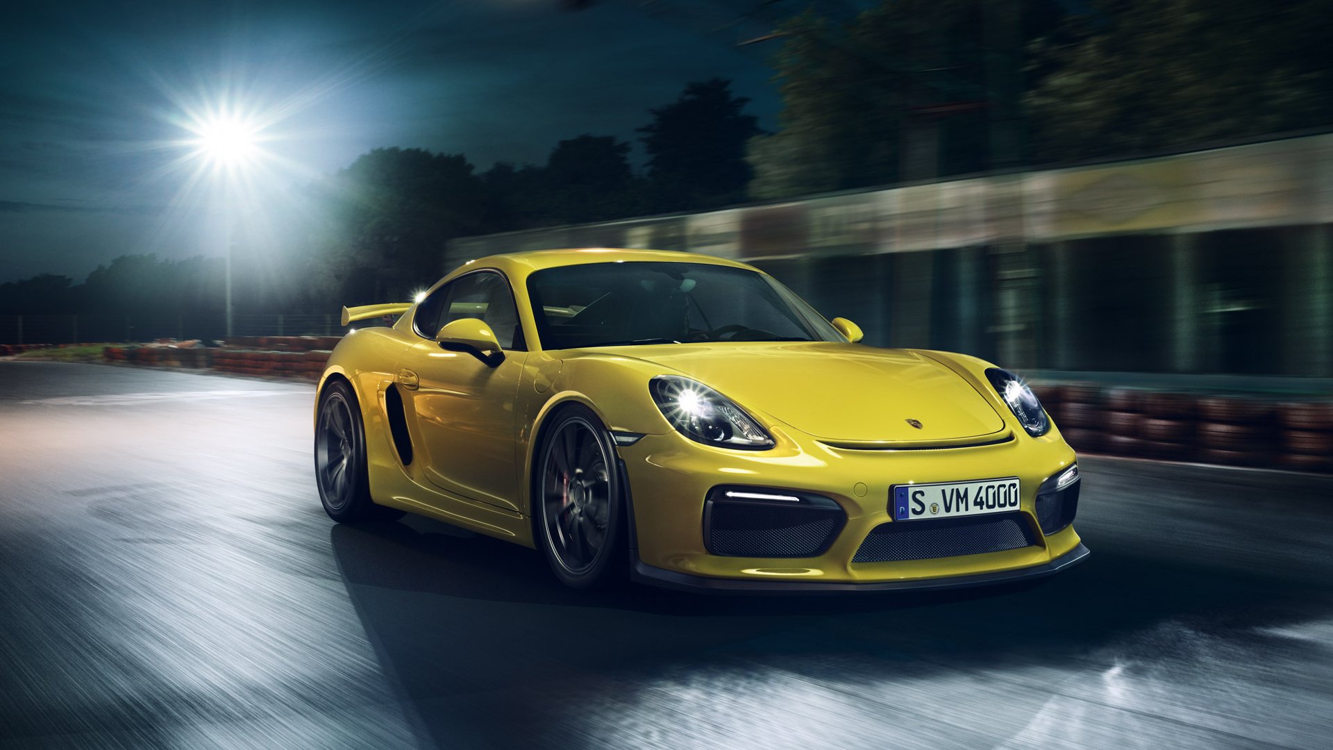 Yellow Porsche Cayman GT4 sports car speeding on a wet road at night, captured in a dynamic HD desktop wallpaper.