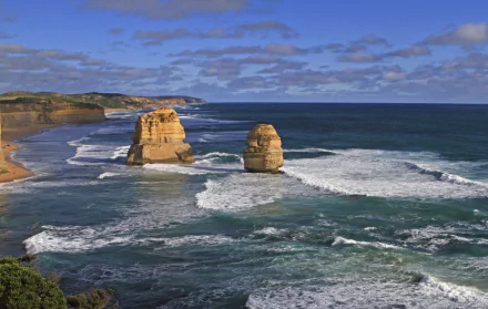A stunning 4K Ultra HD view of The Twelve Apostles limestone stacks along the rugged coastline of Victoria, Australia, with waves crashing beneath a partly cloudy sky.