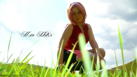 HD desktop wallpaper featuring a woman in cosplay crouching in a grassy field under a bright, partly cloudy sky.