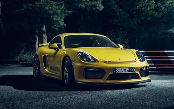 HD desktop wallpaper featuring a sleek yellow Porsche Cayman GT4 parked on a dark road, showcasing the car's sporty design and vibrant color.