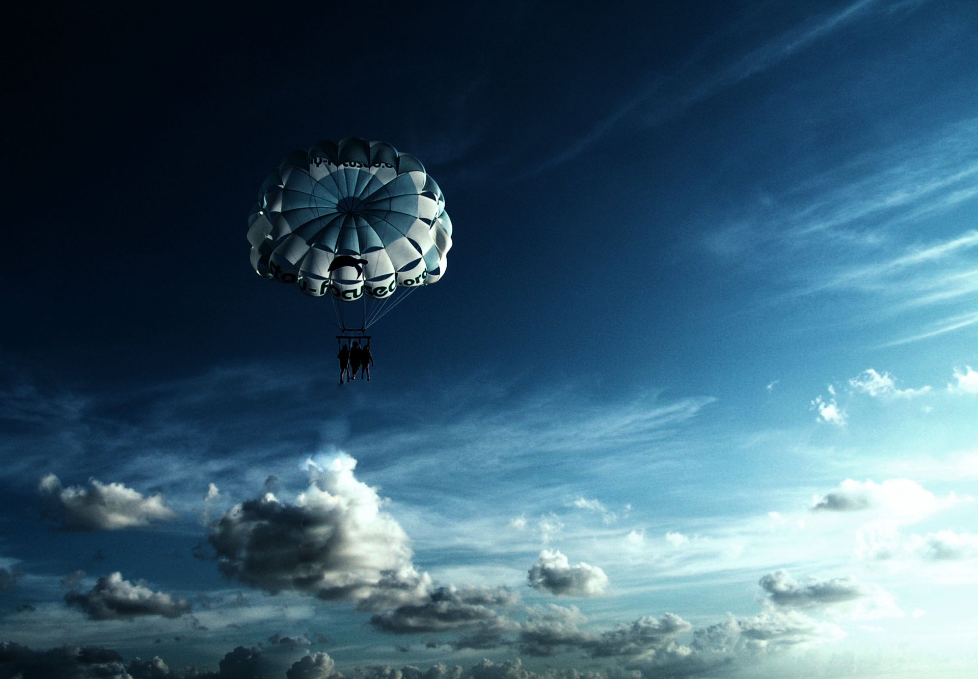 A striking HD wallpaper featuring a military parachute descending against a backdrop of vast blue skies and fluffy clouds, capturing a moment of adventure and exploration.