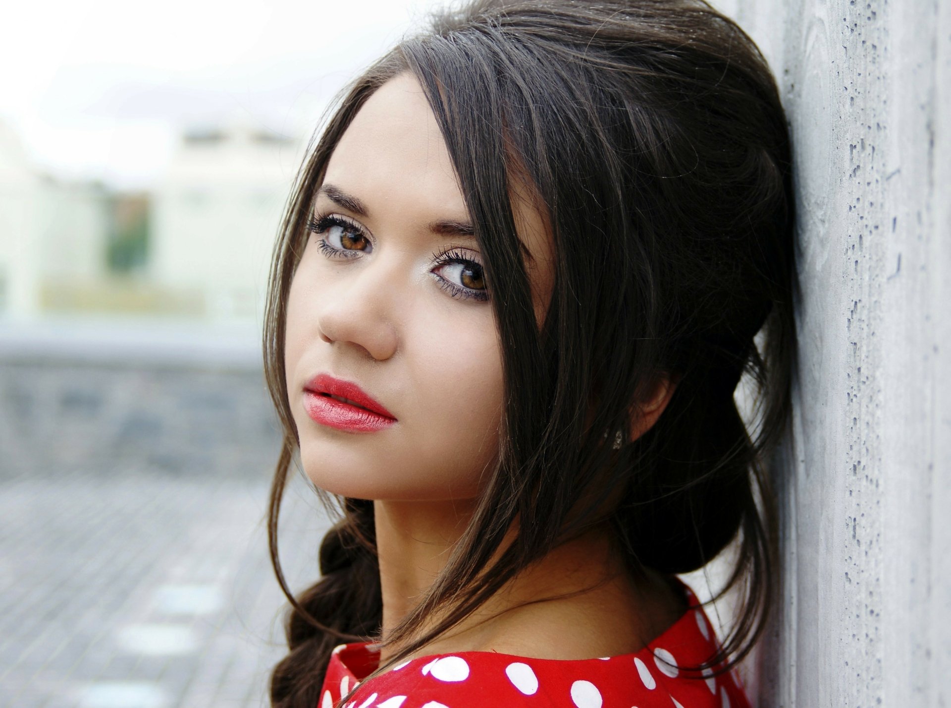 A high-definition portrait wallpaper of a brunette woman with brown eyes and a braid, leaning against a wall.