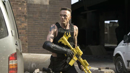 Ninja from the movie Chappie, portrayed by Watkin Tudor Jones, holding a yellow firearm in an urban setting, featured in an HD PC desktop wallpaper.