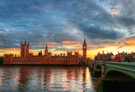 A stunning sunset over the Palace of Westminster and Big Ben, casting vibrant colors across the sky and reflecting on the water, complemented by the iconic bridge in the foreground.