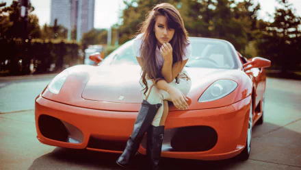 A woman with brown hair, wearing boots, sits on the hood of a red Ferrari in an urban setting. The image serves as an HD desktop wallpaper and background.