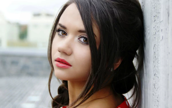 A high-definition portrait wallpaper of a brunette woman with brown eyes and a braid, leaning against a wall.