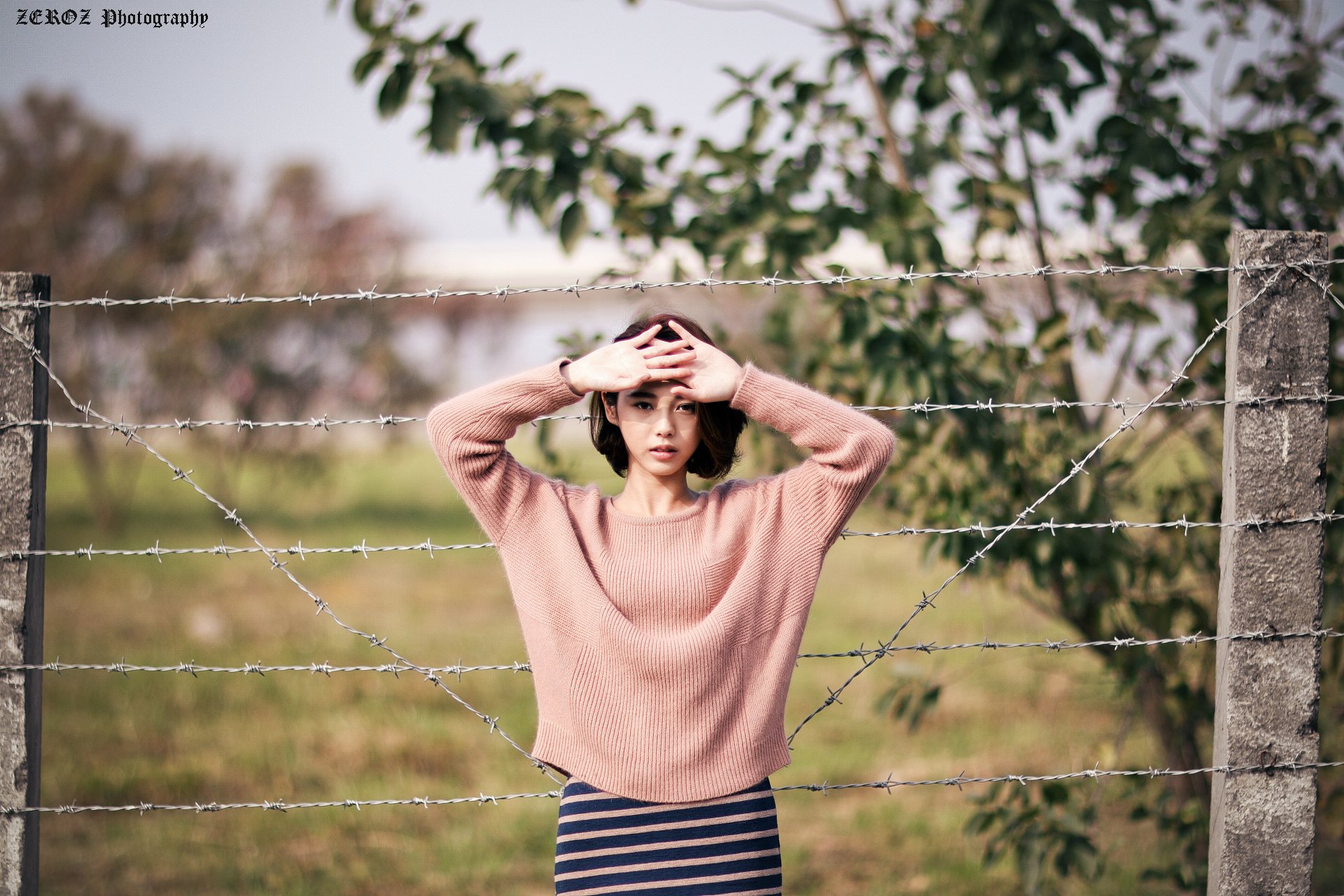 HD wallpaper featuring Taiwanese model Lín Yǔ posing behind barbed wire with a soft bokeh background in a natural outdoor setting.