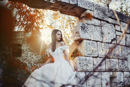 A brunette bride with brown eyes wearing a wedding dress poses amidst rustic stone ruins, bathed in warm sunlight, captured in an HD PC desktop wallpaper.