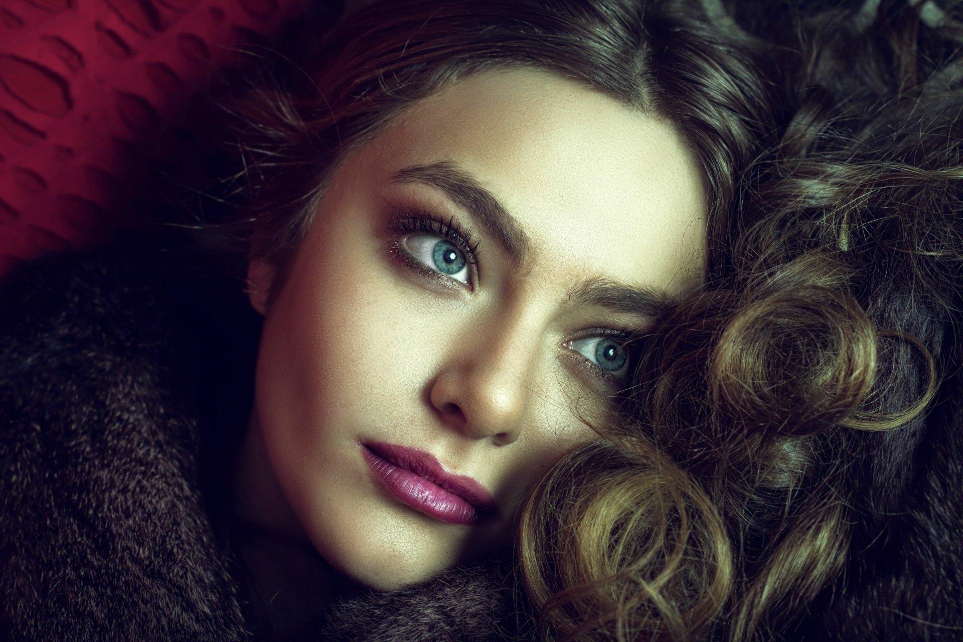 Close-up 4K Ultra HD portrait of a brunette woman with blue eyes and bold lipstick, showcasing her face with soft lighting and detailed texture.