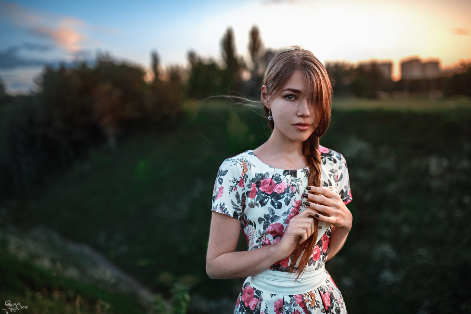 A blonde woman in a floral dress stands outdoors, her hair styled in a braid, against a backdrop of sunset and greenery. This HD image serves as a vibrant desktop wallpaper.