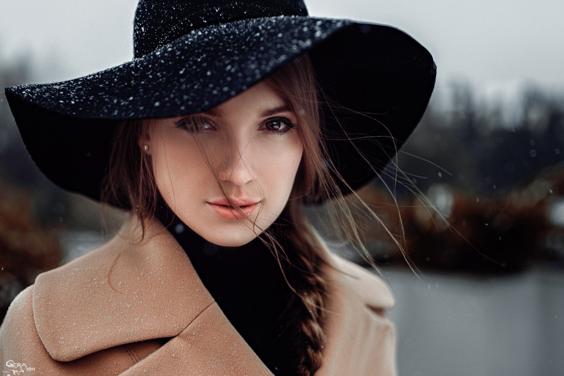 A brunette woman with brown eyes and a braided hairstyle wears a wide-brimmed black hat, set against a moody, rainy background in this HD desktop wallpaper.