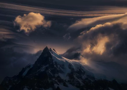 Majestic Patagonia mountain peaks tower beneath dynamic clouds, while a bird soars through the snowy landscape, capturing the serene beauty of nature in this stunning HD wallpaper.