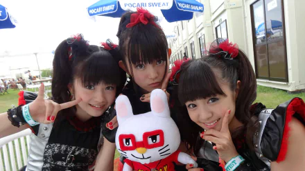 Three girls in stylish outfits pose with a plush toy, showcasing their heavy metal influence as members of Babymetal. Bright and vibrant, this HD image reflects Asian music culture.