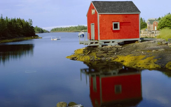A vibrant red building reflects in calm water, surrounded by lush greenery and a serene Canadian landscape, showcasing man-made beauty against a tranquil backdrop.