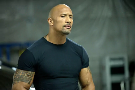 HD desktop wallpaper: muscular bald actor in a black tee, intense expression on an industrial set, evoking the action movie San Andreas.