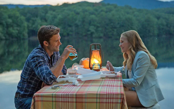 HD desktop wallpaper from the movie The Longest Ride, showing a romantic outdoor dinner by a lake with a couple sharing a cozy moment at sunset.