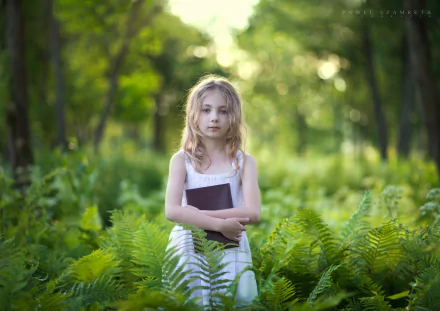 Blue-eyed blonde child in a white dress holding a book among lush ferns, soft bokeh forest photography — HD PC desktop wallpaper/background