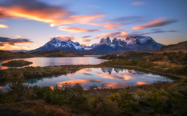 A stunning landscape of Torres del Paine in Chile, featuring dramatic mountains and a tranquil lake reflecting the colorful sky, showcasing the natural beauty of Patagonia.