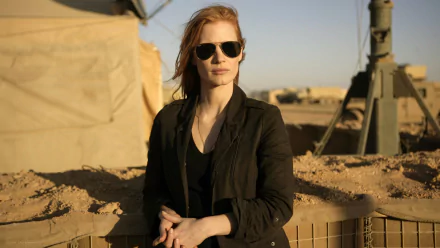 Jessica Chastain in character from the movie Zero Dark Thirty, standing outdoors in desert-like terrain, wearing dark sunglasses and a black jacket.