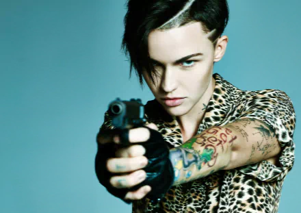 HD desktop wallpaper featuring celebrity Ruby Rose pointing a gun, showcasing a fierce look with tattoos and a leopard print shirt.