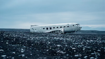A weathered aircraft wreck lies on a stark, black landscape under a cloudy sky, creating a striking contrast in this HD PC desktop wallpaper.