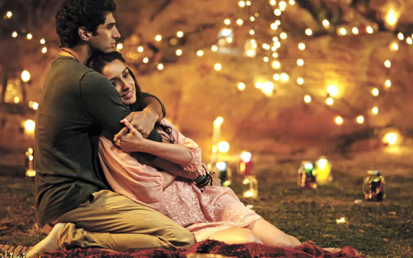 A romantic moment from the movie Aashiqui 2 featuring a couple hugging outdoors, surrounded by glowing lights, in a HD desktop wallpaper background.