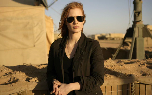 Jessica Chastain in character from the movie Zero Dark Thirty, standing outdoors in desert-like terrain, wearing dark sunglasses and a black jacket.