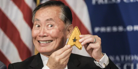 HD desktop wallpaper featuring George Takei holding a Star Trek insignia with a joyful expression, against a backdrop with the American flag.