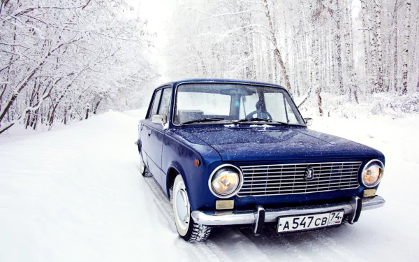 HD desktop wallpaper featuring a classic blue Lada vehicle parked on a snowy road surrounded by snow-covered trees in a winter forest setting.
