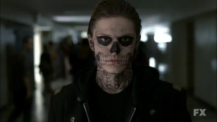 Evan Peters in character from TV show American Horror Story, with dark eye makeup and skull-themed face paint, standing in a dimly lit corridor. HD desktop wallpaper and background.