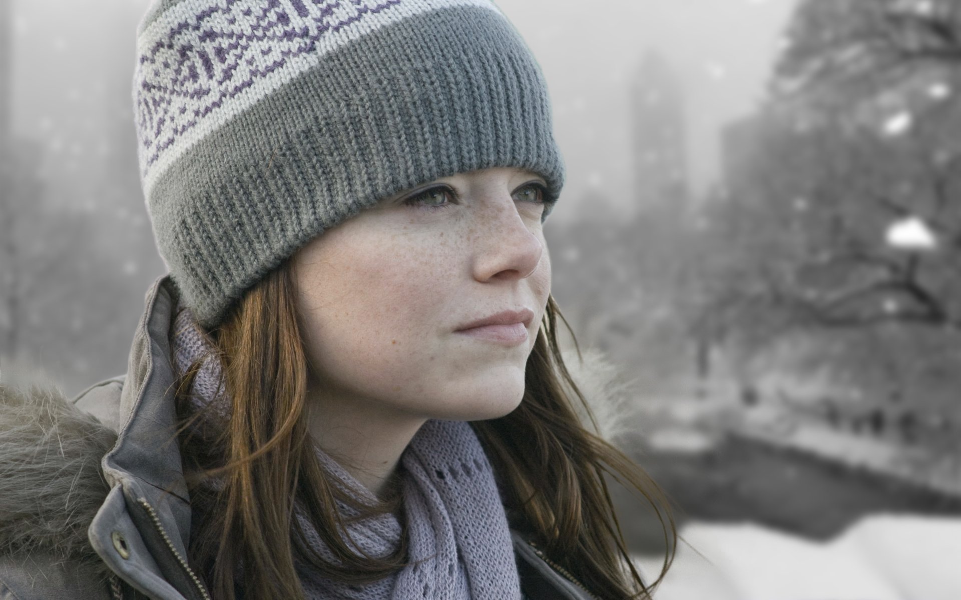 Close-up of an actress from the movie Paper Man wearing a knit hat and scarf, gazing across a snowy urban park — HD PC desktop wallpaper.
