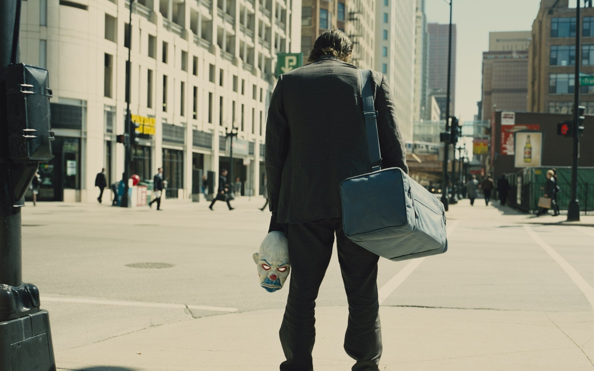 2K Quad HD PC desktop wallpaper: rear view of a suited figure carrying a duffel and a clown mask while walking down a city street, scene from the movie The Dark Knight.