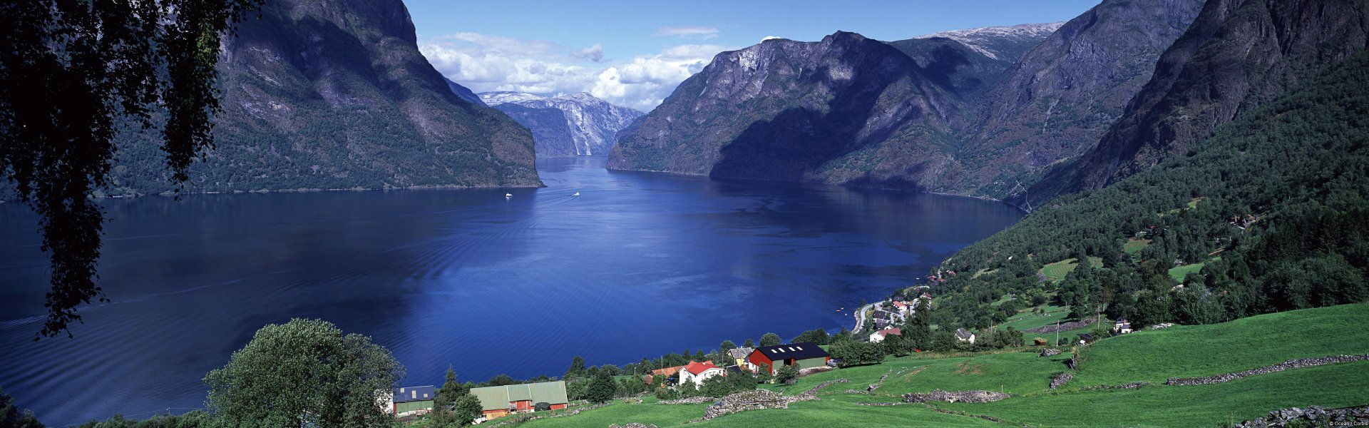 Scenic view of Aurlandsfjord in Norway, showcasing steep mountains and calm blue waters under a partly cloudy sky, captured in high-definition landscape photography.
