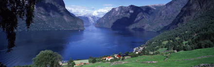 Scenic view of Aurlandsfjord in Norway, showcasing steep mountains and calm blue waters under a partly cloudy sky, captured in high-definition landscape photography.