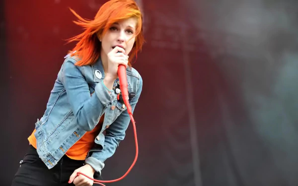 Vibrant HD PC desktop wallpaper: female rock singer with bright orange hair gripping a red microphone on a smoky stage — music background.