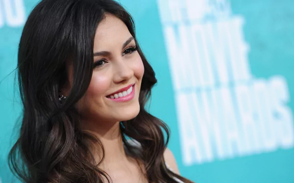 Smiling young woman with long dark hair against a turquoise event backdrop — 2K Quad HD PC desktop wallpaper/background.