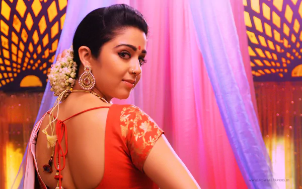 HD PC wallpaper of a film actress in a red sari, glancing over her shoulder on a colorful stage set from the movie Jyothi Lakshmi.