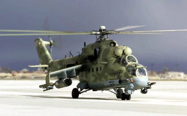 HD desktop wallpaper showing a military Mil Mi-24 helicopter on a runway with rotors spinning against a muted sky background.