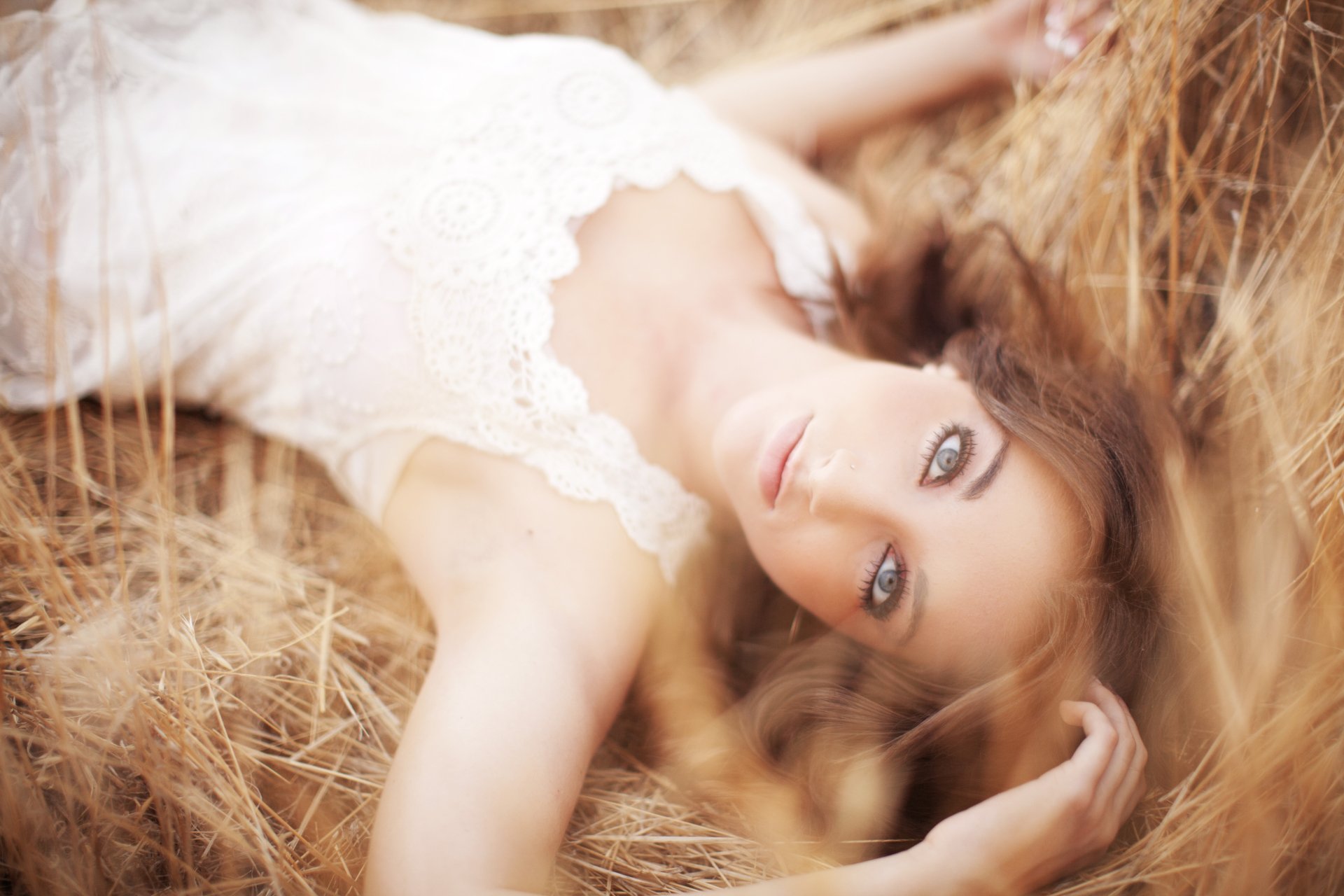 A 4K Ultra HD desktop wallpaper featuring a woman model lying in dry grass, wearing a white lace dress, with soft natural lighting and a dreamy expression.