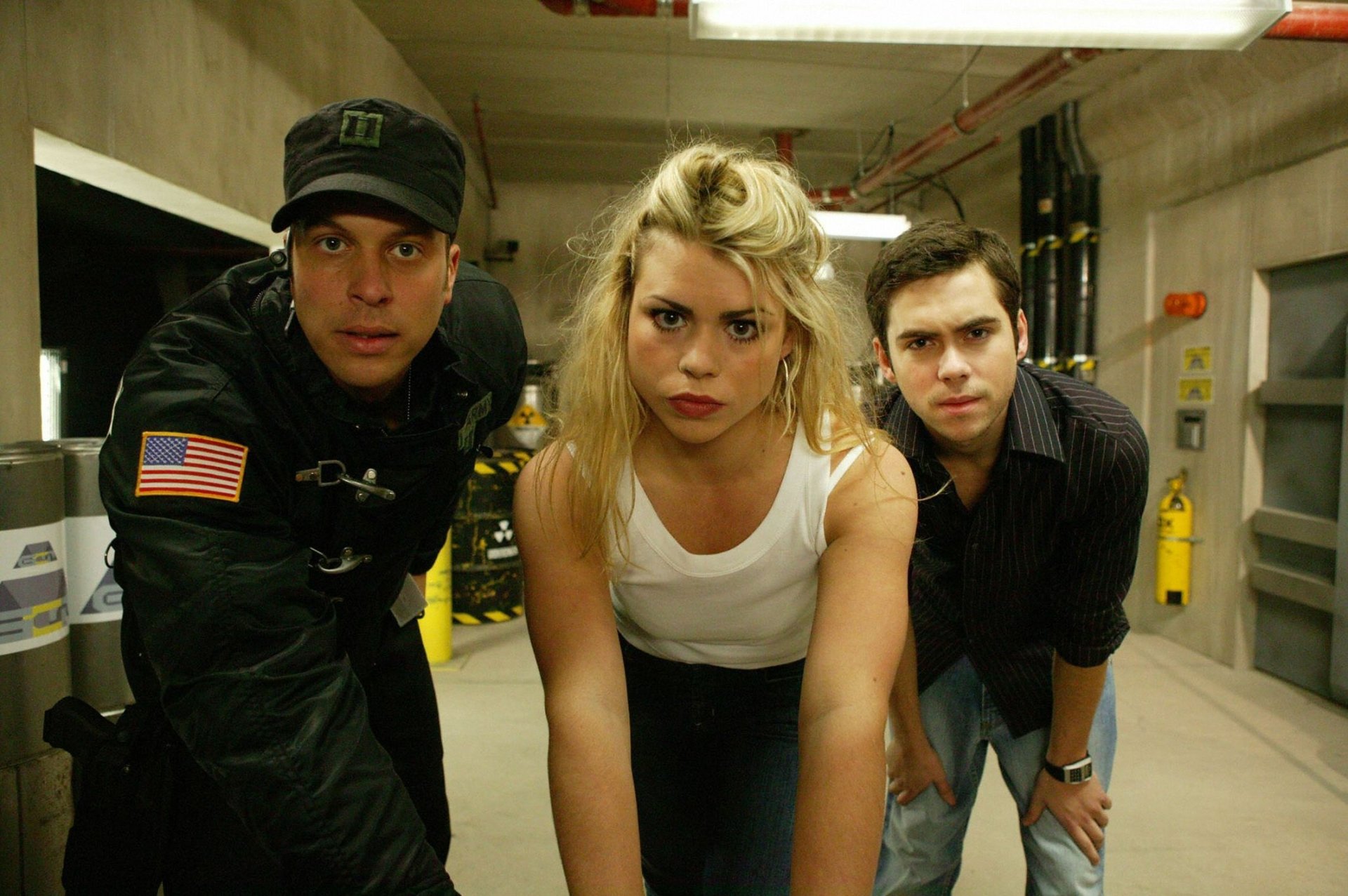 HD PC desktop wallpaper: three Doctor Who (2005) characters — a woman in a white tank top flanked by two men, leaning forward in a concrete corridor, alert and ready for action.