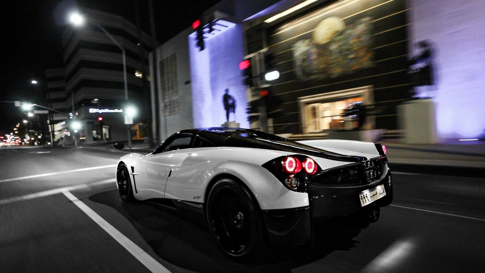 HD PC desktop wallpaper featuring a sleek Pagani Huayra vehicle driving at night in an urban setting.