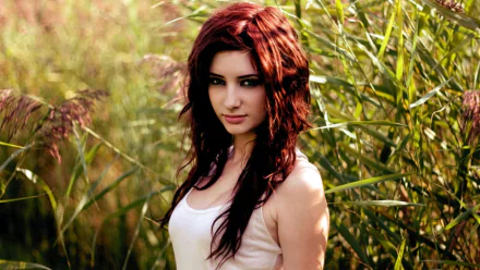HD PC desktop wallpaper featuring celebrity Susan Coffey standing outdoors amidst tall green grasses, with sunlight highlighting her red hair and white top.