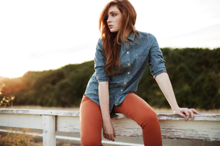 5K Ultra HD PC desktop wallpaper of a red-haired woman model in a denim shirt and rust pants perched on a white fence at sunset.